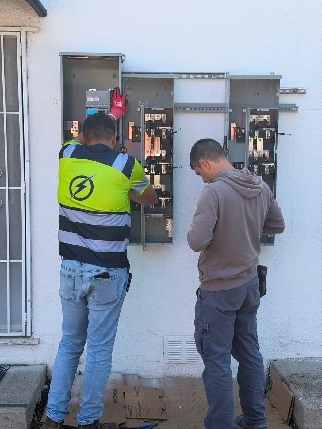 Electricians installing new panel and meter enclosures on exterior wall