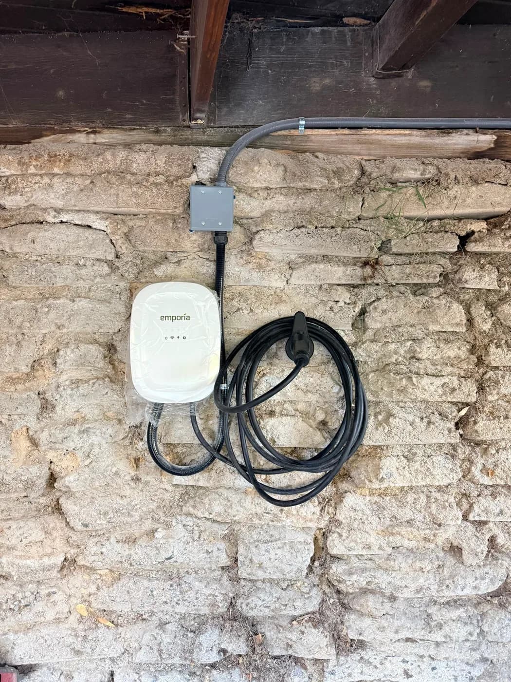 Emporia EV charger mounted on stone wall with charging cable coiled below