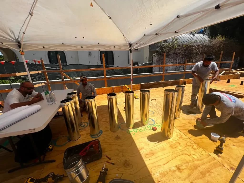 HVAC crew installing round vent flue pipes on a rooftop deck