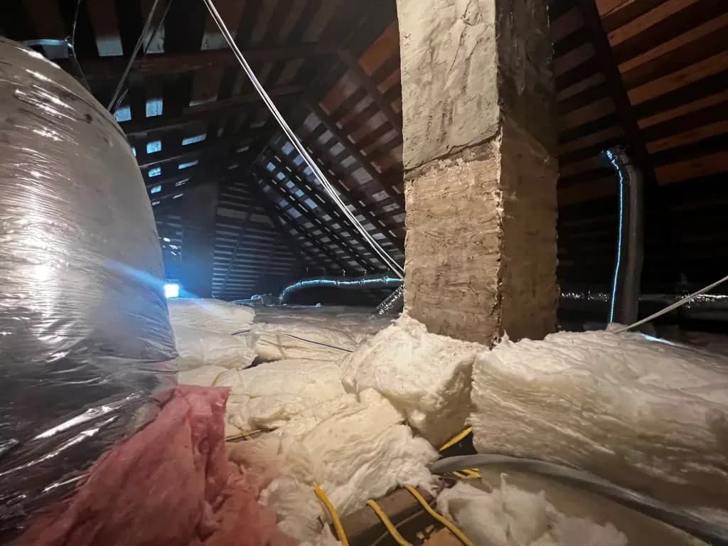 Attic insulation with flexible HVAC ductwork running past the roof rafters