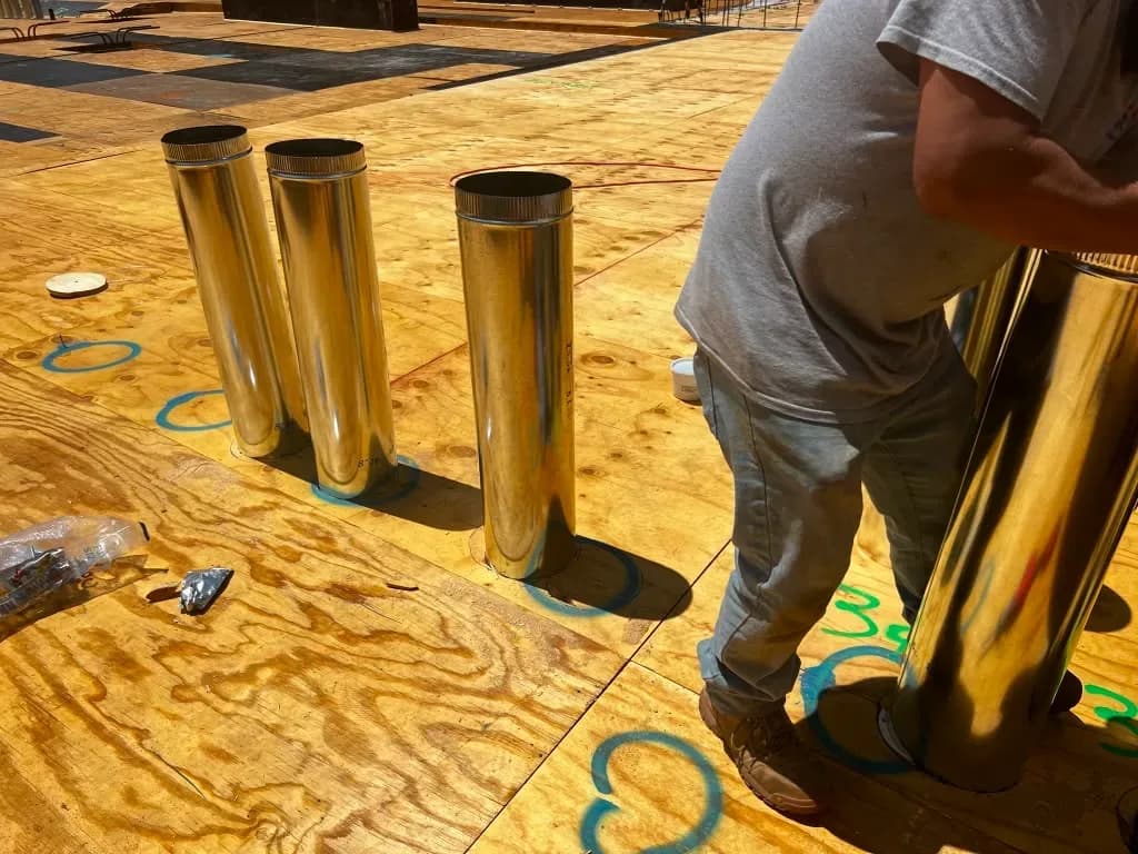 Worker installing a row of galvanized flue vent pipes on a commercial roof deck