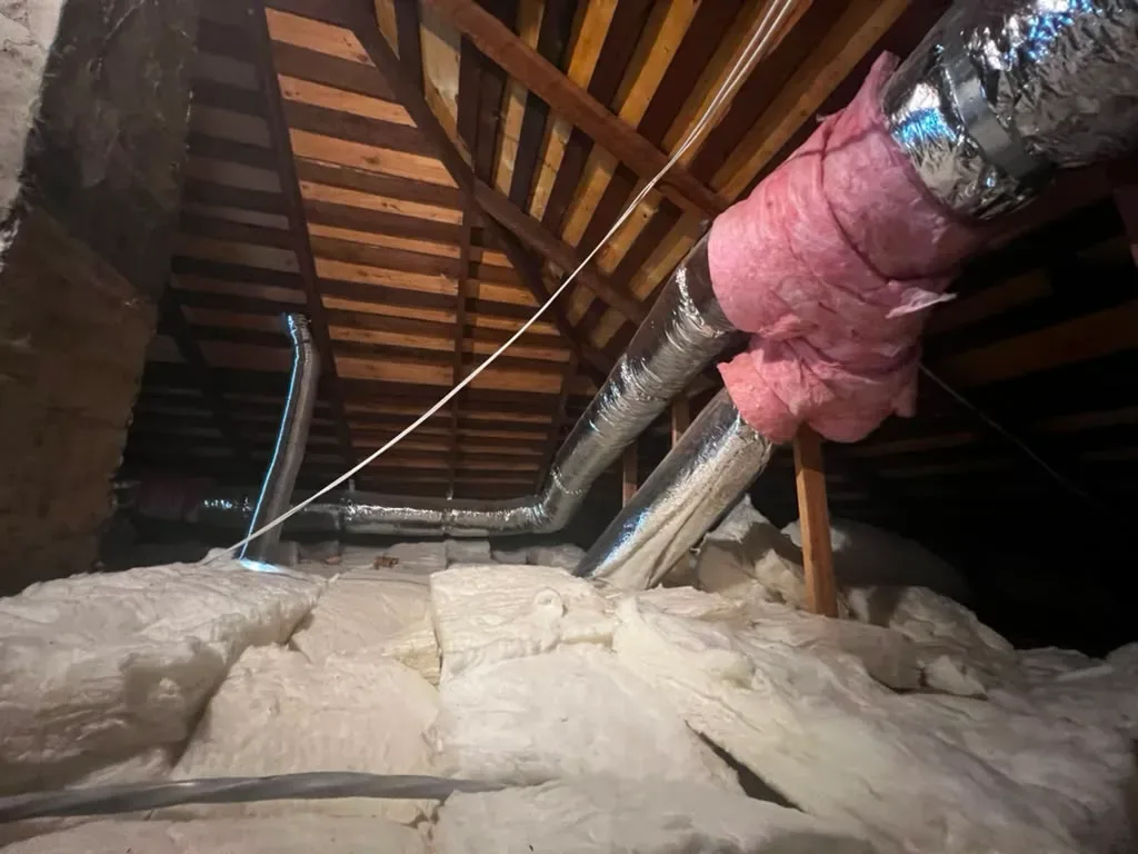 Attic ductwork trunk line wrapped in pink fiberglass insulation