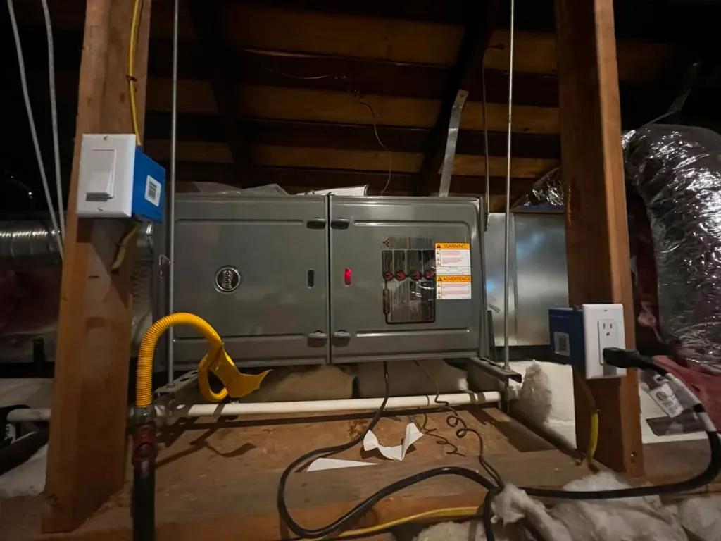 Gray furnace or air handler cabinet installed in attic with electrical disconnects