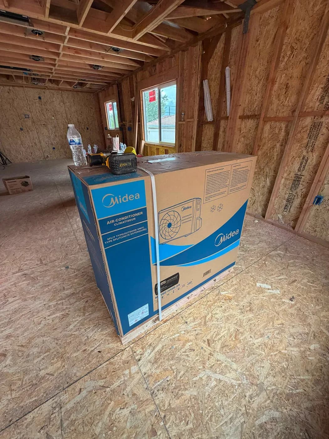 Boxed Midea split air conditioner outdoor unit staged inside a home under construction