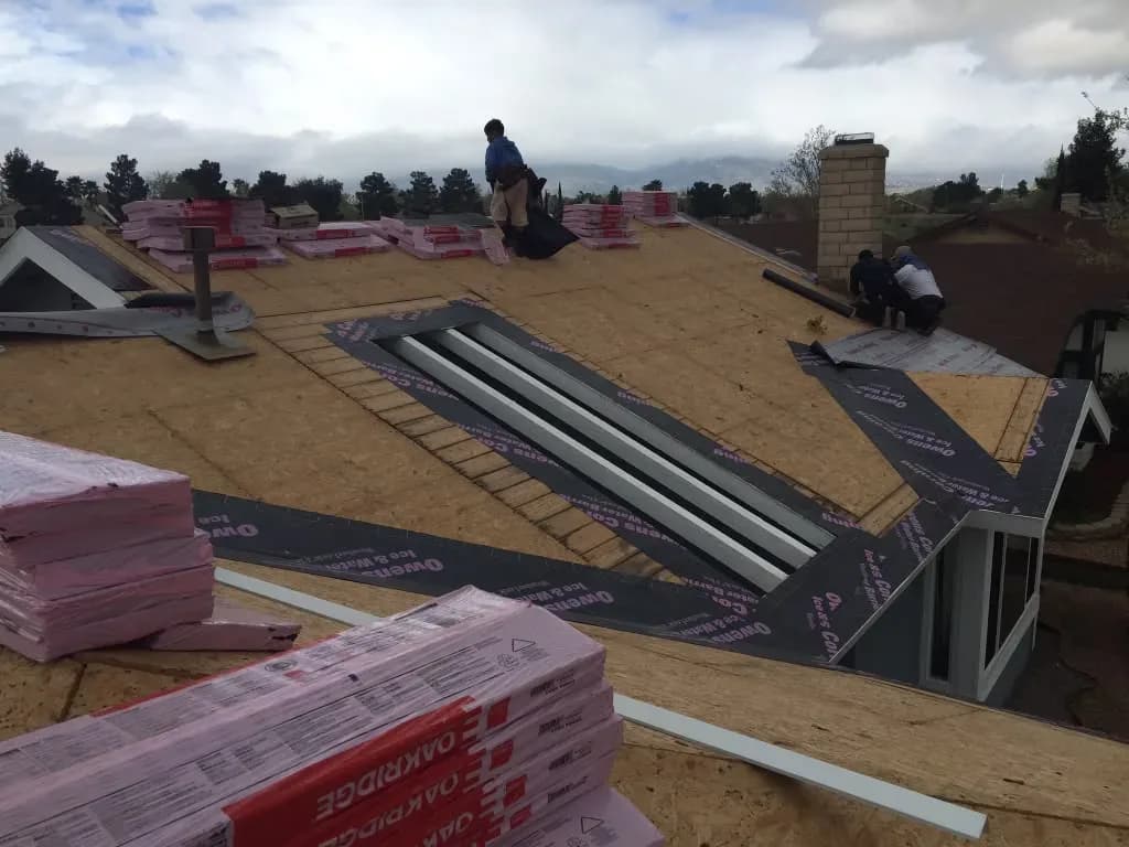 Aerial view of roof deck with new underlayment, skylight curb installation, and stacked shingle bundles