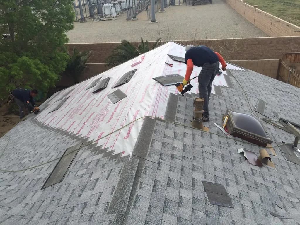 Two roofers installing new asphalt shingles on a hip roof with a nail gun