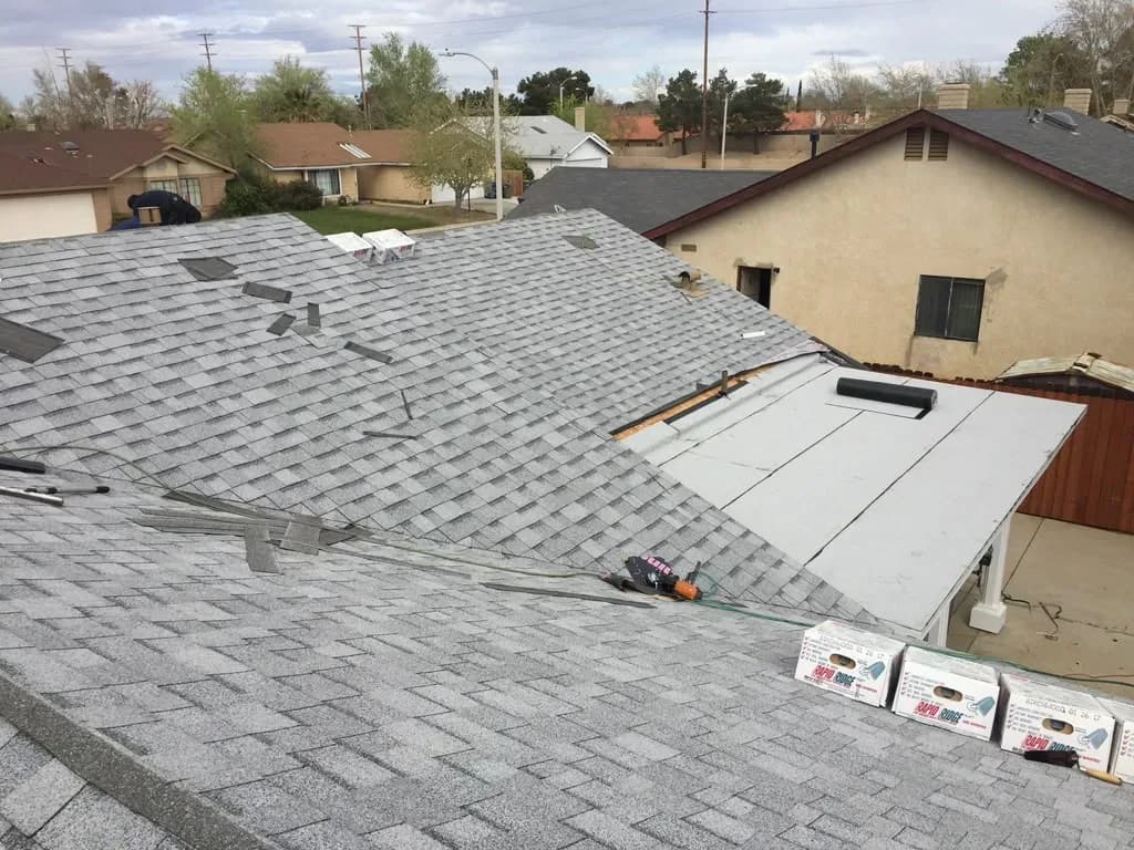 Nearly finished shingle roof with ridge cap boxes staged and a flat patio roof section in view