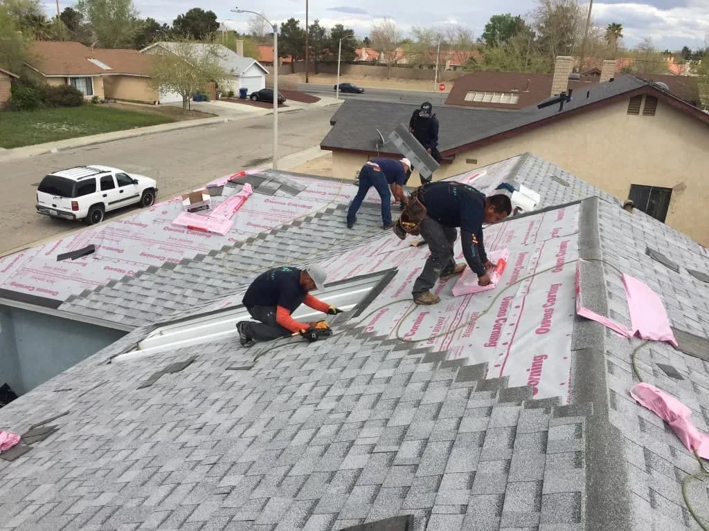Four-person roofing crew installing shingles across a large roof section