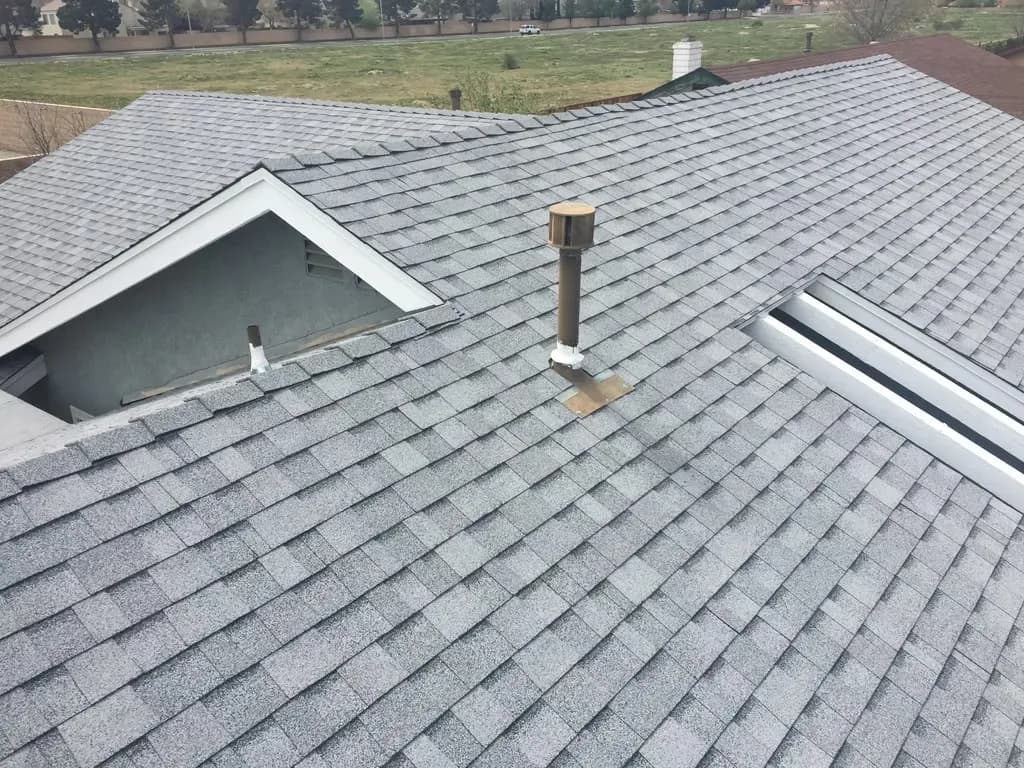 Aerial view of a finished gray asphalt shingle roof with vent pipe and skylight edge