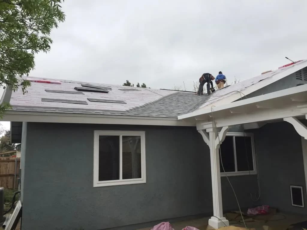 Roofing crew installing underlayment on a gray stucco home's roof