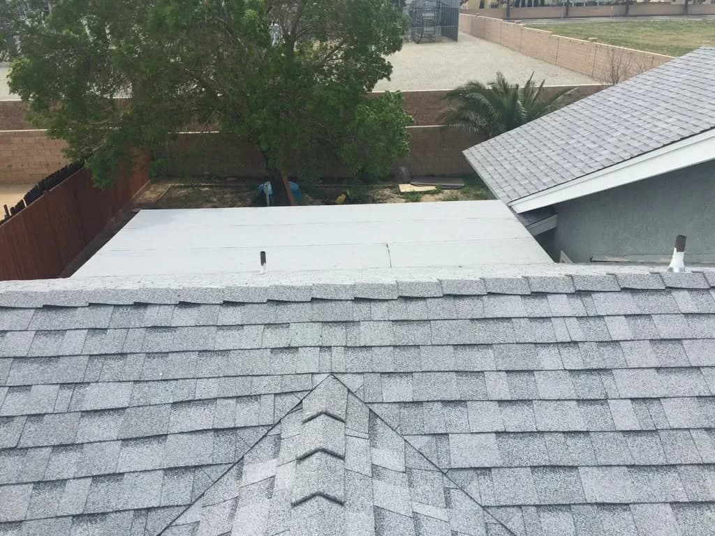 Completed shingle roof adjoining a flat roof section with backyard view