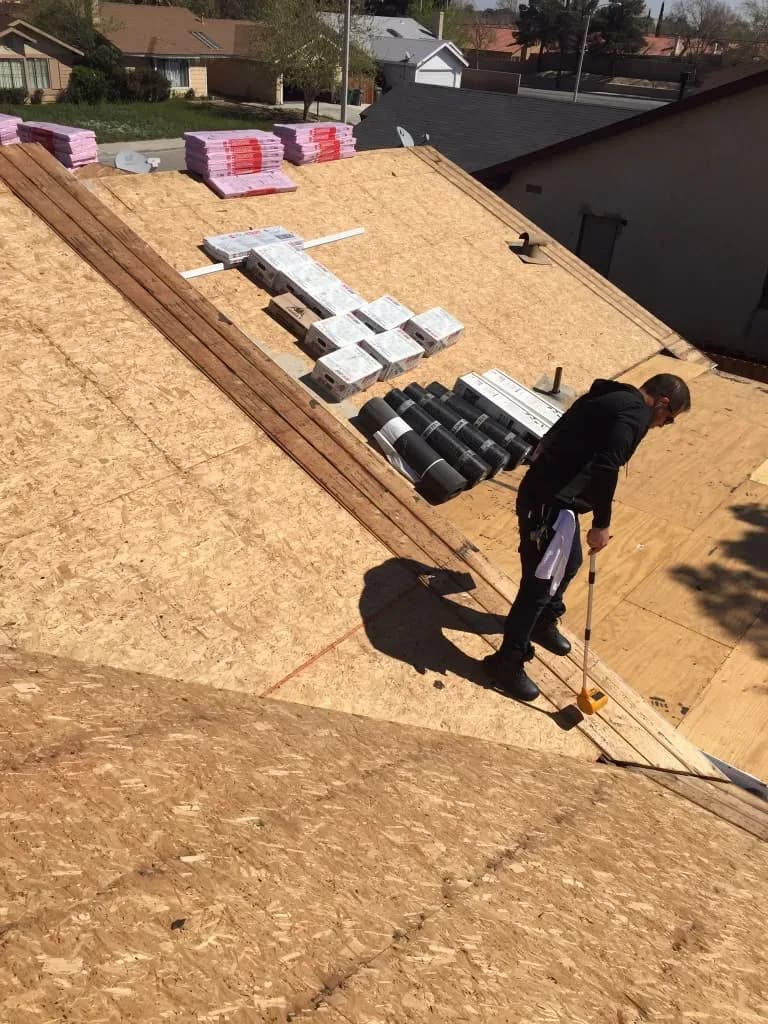 Worker measuring roof decking with shingle bundles and insulation staged for installation